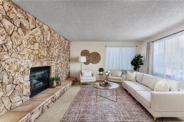 living room featuring a stone fireplace, carpet floors, and a textured ceiling