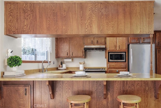 kitchen with appliances with stainless steel finishes, a kitchen bar, kitchen peninsula, and sink