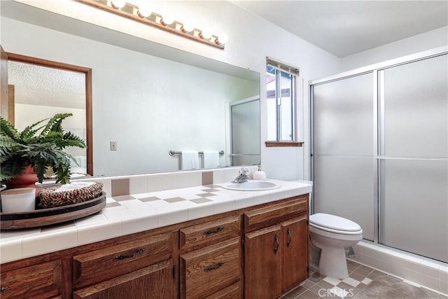 bathroom featuring a shower with door, vanity, tile patterned floors, and toilet