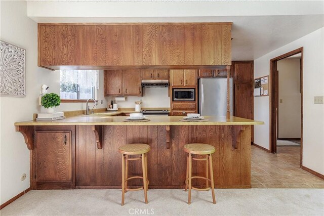 kitchen with sink, a breakfast bar area, light tile patterned floors, kitchen peninsula, and stainless steel appliances