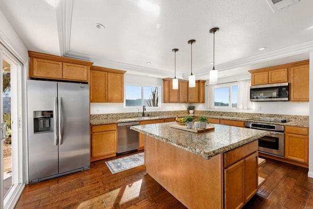 kitchen with dark wood-type flooring, a center island, appliances with stainless steel finishes, pendant lighting, and light stone countertops