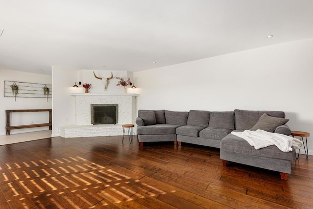 living room with a brick fireplace and dark wood-type flooring