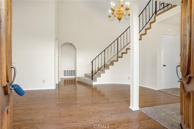 foyer entrance with hardwood / wood-style floors, a towering ceiling, and a chandelier