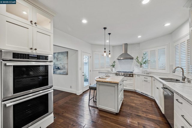 kitchen featuring appliances with stainless steel finishes, sink, white cabinets, a center island, and wall chimney range hood