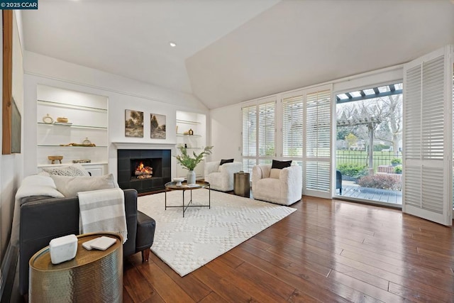 living room with lofted ceiling, a tiled fireplace, built in features, and dark hardwood / wood-style floors