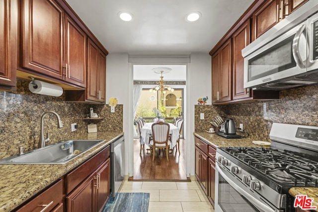 kitchen with sink, dark stone counters, light tile patterned floors, a notable chandelier, and stainless steel appliances