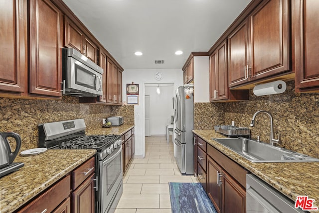 kitchen featuring sink, light stone counters, light tile patterned floors, appliances with stainless steel finishes, and backsplash