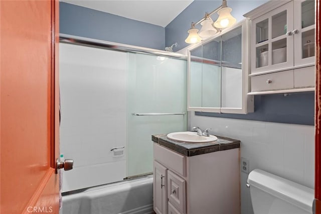 full bathroom with enclosed tub / shower combo, tile walls, vanity, and toilet