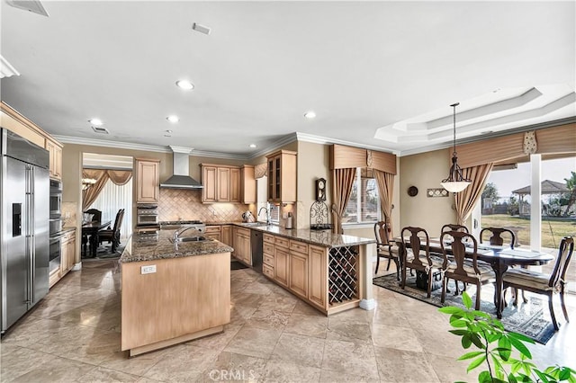 kitchen with tasteful backsplash, an island with sink, dark stone countertops, hanging light fixtures, and wall chimney exhaust hood