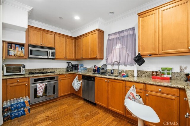 kitchen with sink, appliances with stainless steel finishes, light stone counters, ornamental molding, and light hardwood / wood-style floors