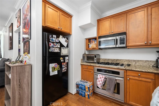 kitchen with light stone countertops, ornamental molding, stainless steel appliances, and light wood-type flooring