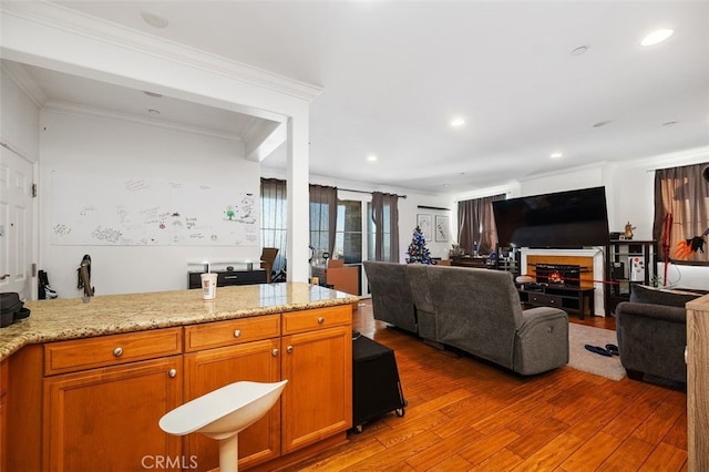 kitchen with wood-type flooring, ornamental molding, and light stone counters