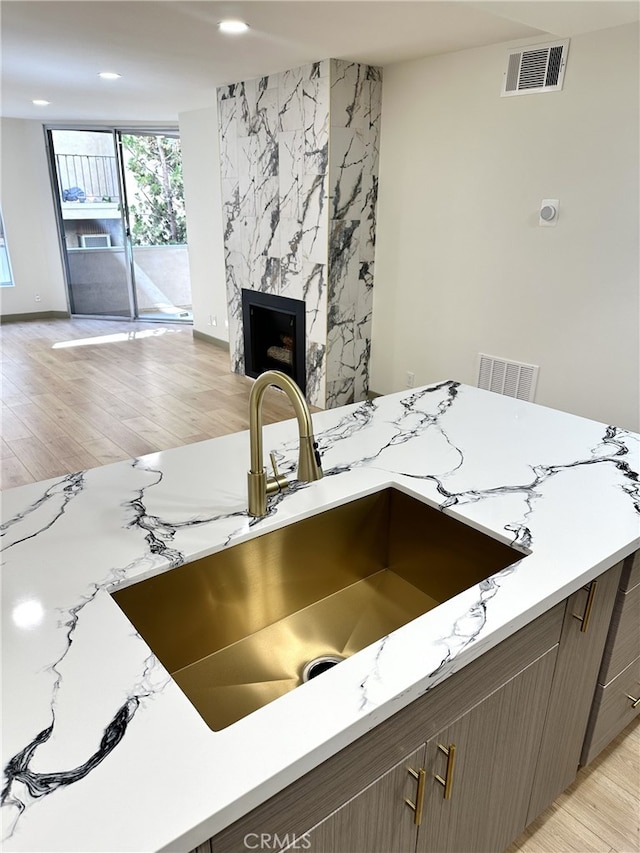 interior details featuring sink, light stone counters, dark brown cabinets, a fireplace, and light hardwood / wood-style floors