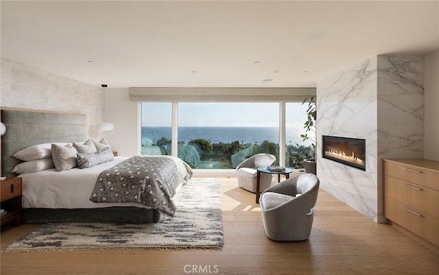 bedroom featuring a premium fireplace, a water view, and light hardwood / wood-style flooring