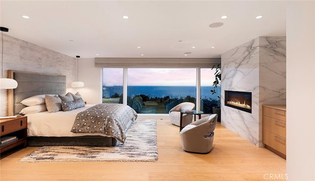 bedroom with a water view, a fireplace, light hardwood / wood-style flooring, and access to outside