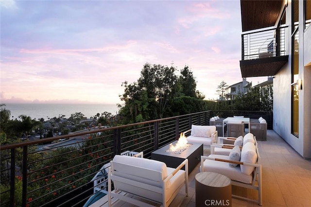 patio terrace at dusk with a balcony, a water view, and an outdoor living space with a fire pit