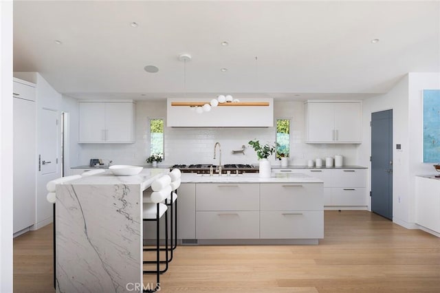 kitchen featuring white cabinetry, sink, decorative backsplash, and a center island with sink