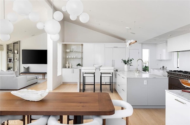 kitchen with sink, white cabinetry, double oven range, hanging light fixtures, and an island with sink