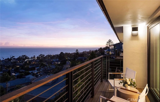 balcony at dusk featuring a water view