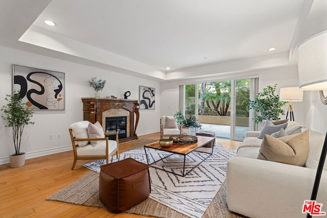 living room with hardwood / wood-style floors, a tray ceiling, and a premium fireplace