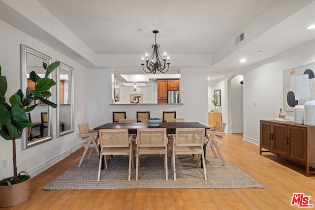 dining room with a notable chandelier, light hardwood / wood-style flooring, and a raised ceiling