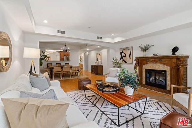 living room with a high end fireplace, a chandelier, and light hardwood / wood-style floors