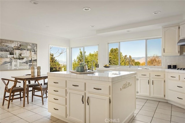 kitchen with tile countertops, tasteful backsplash, sink, white cabinets, and light tile patterned floors