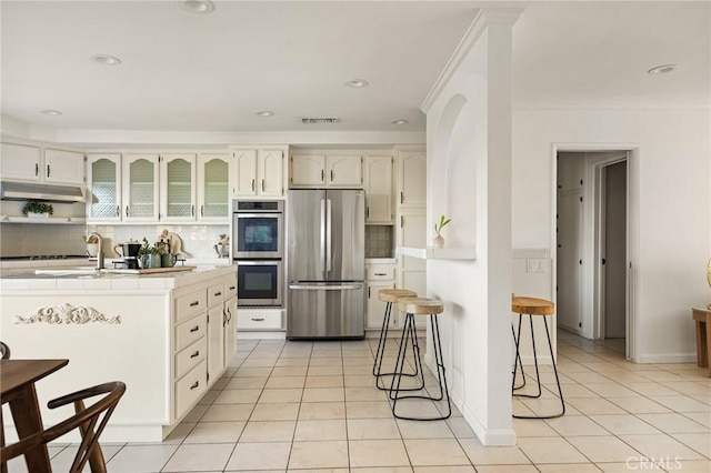 kitchen with tasteful backsplash, light tile patterned floors, stainless steel appliances, and a kitchen breakfast bar