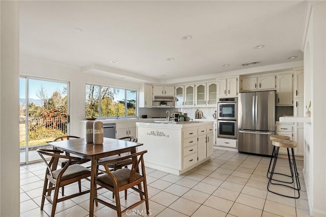 kitchen featuring tasteful backsplash, light tile patterned flooring, appliances with stainless steel finishes, and a center island with sink