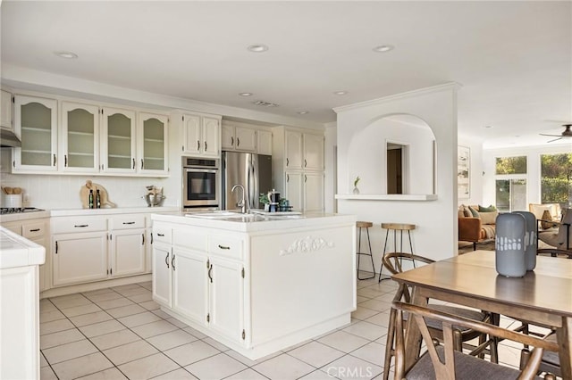 kitchen featuring light tile patterned floors, ceiling fan, stainless steel appliances, a kitchen island with sink, and backsplash