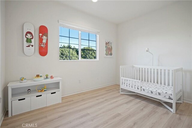 bedroom with light wood-type flooring and a crib