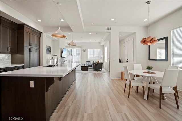 kitchen with pendant lighting, sink, dark brown cabinets, light hardwood / wood-style floors, and a large island with sink