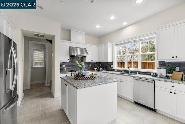 kitchen with extractor fan, a kitchen island, appliances with stainless steel finishes, white cabinetry, and light stone counters