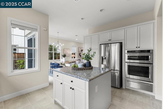 kitchen with appliances with stainless steel finishes, stone countertops, pendant lighting, white cabinetry, and a center island