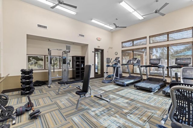 exercise room with ceiling fan, carpet flooring, and a towering ceiling