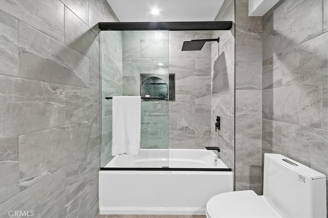 bathroom with tile walls, shower / bath combination with glass door, and toilet