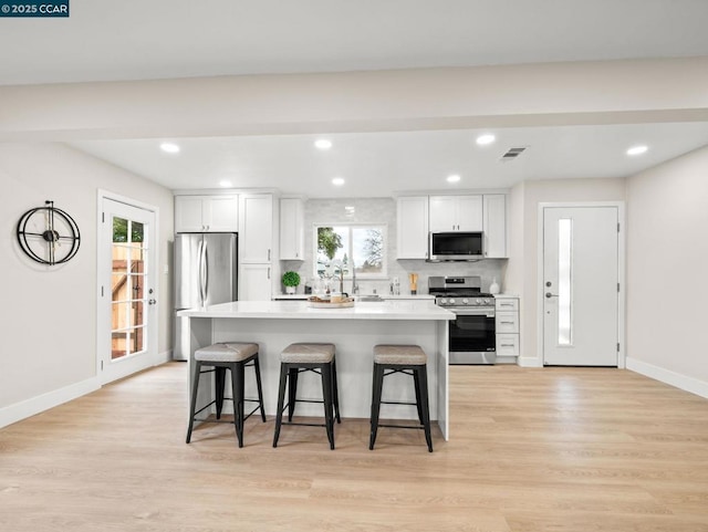 kitchen with white cabinetry, a kitchen breakfast bar, a center island, stainless steel appliances, and light wood-type flooring