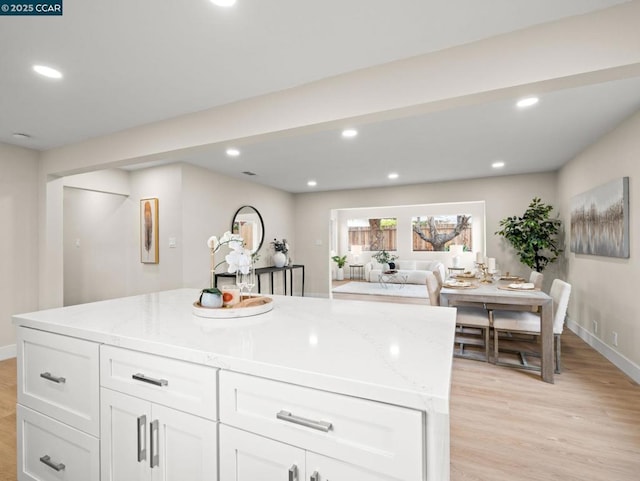 kitchen with light hardwood / wood-style flooring, light stone countertops, white cabinets, and a kitchen island