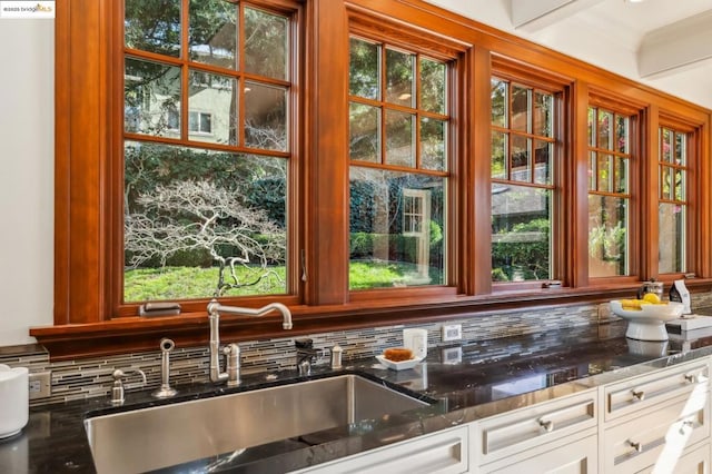 kitchen featuring sink, white cabinetry, crown molding, dark stone counters, and backsplash