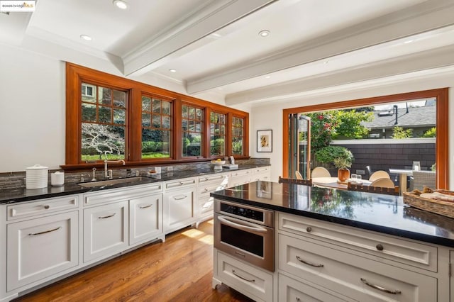 kitchen featuring sink, white cabinetry, beam ceiling, dark stone counters, and stainless steel oven