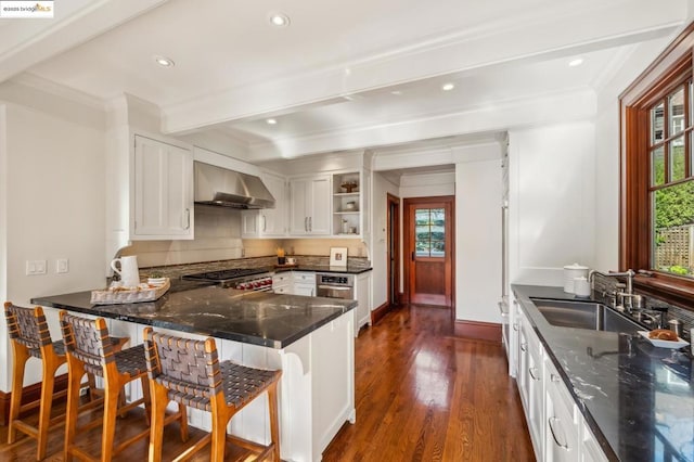 kitchen with a breakfast bar, white cabinetry, sink, kitchen peninsula, and wall chimney range hood