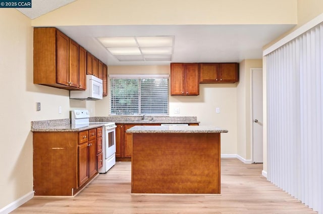 kitchen with white appliances, stone countertops, a kitchen island, and light hardwood / wood-style flooring