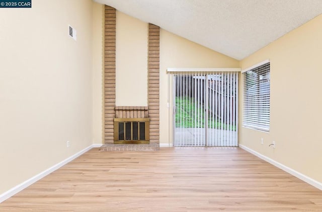 unfurnished living room with a fireplace, vaulted ceiling, light hardwood / wood-style floors, and a textured ceiling