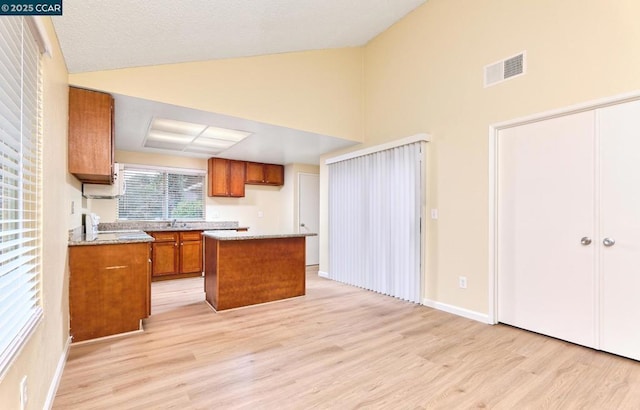 kitchen with high vaulted ceiling, a center island, sink, and light wood-type flooring