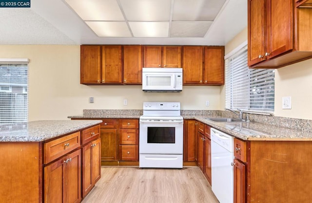 kitchen with light stone counters, white appliances, sink, and light hardwood / wood-style flooring