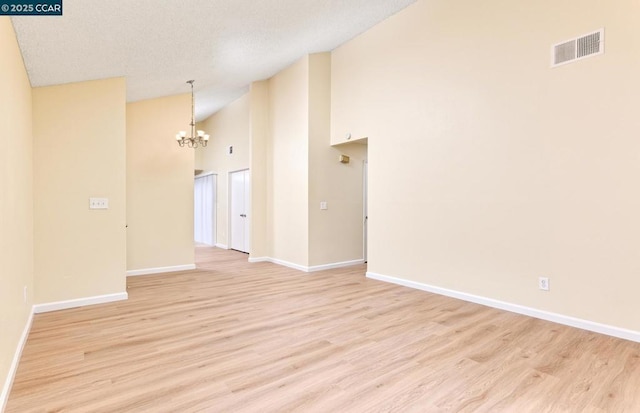 empty room with an inviting chandelier, high vaulted ceiling, light hardwood / wood-style floors, and a textured ceiling