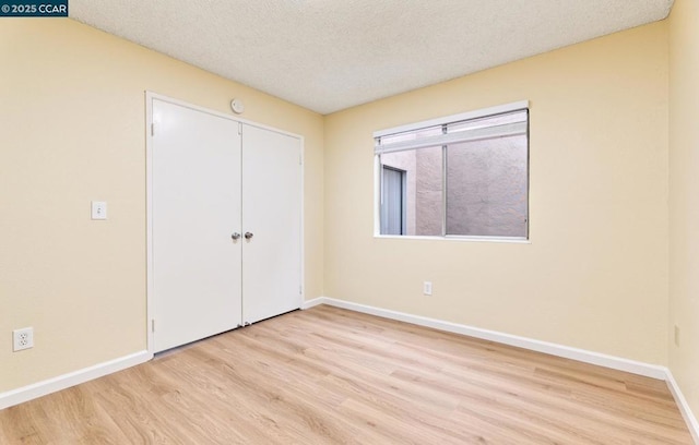 unfurnished bedroom featuring a textured ceiling, light wood-type flooring, and a closet