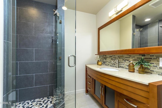 bathroom featuring tile patterned floors, vanity, a shower with door, and decorative backsplash