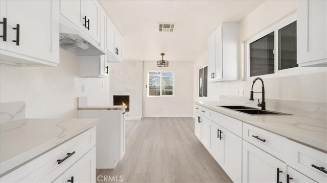 kitchen featuring light stone counters, light wood finished floors, visible vents, white cabinets, and a sink