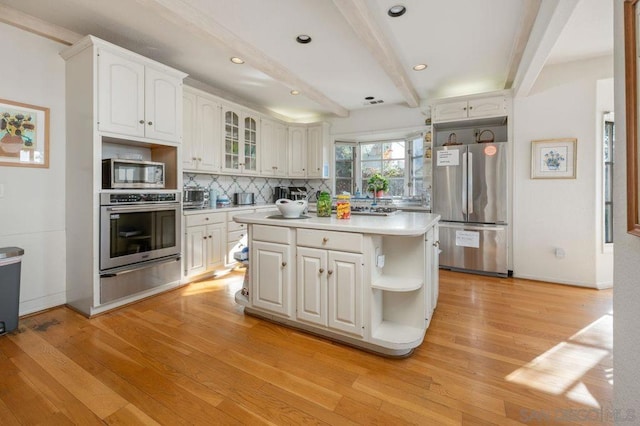 kitchen featuring a center island, light wood-type flooring, appliances with stainless steel finishes, beam ceiling, and white cabinets